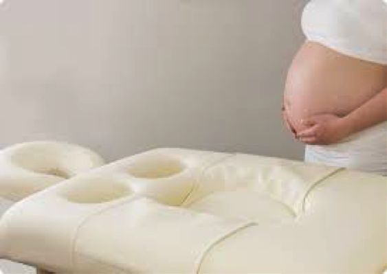 Speciale massagetafel met uitsparing voor buik en borsten, met een zwangere vrouw ernaast